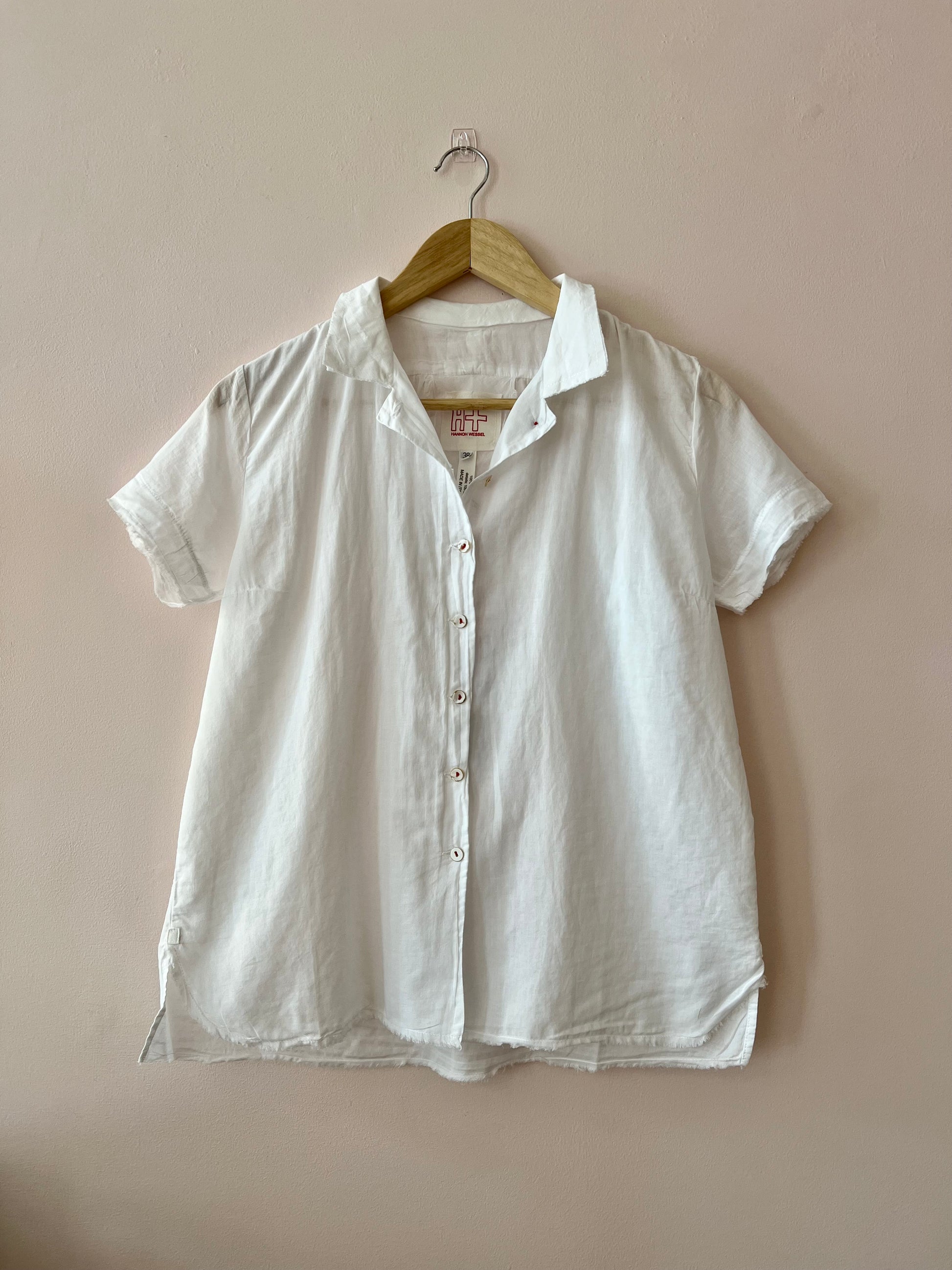 White button-up shirt on a hanger against a beige wall