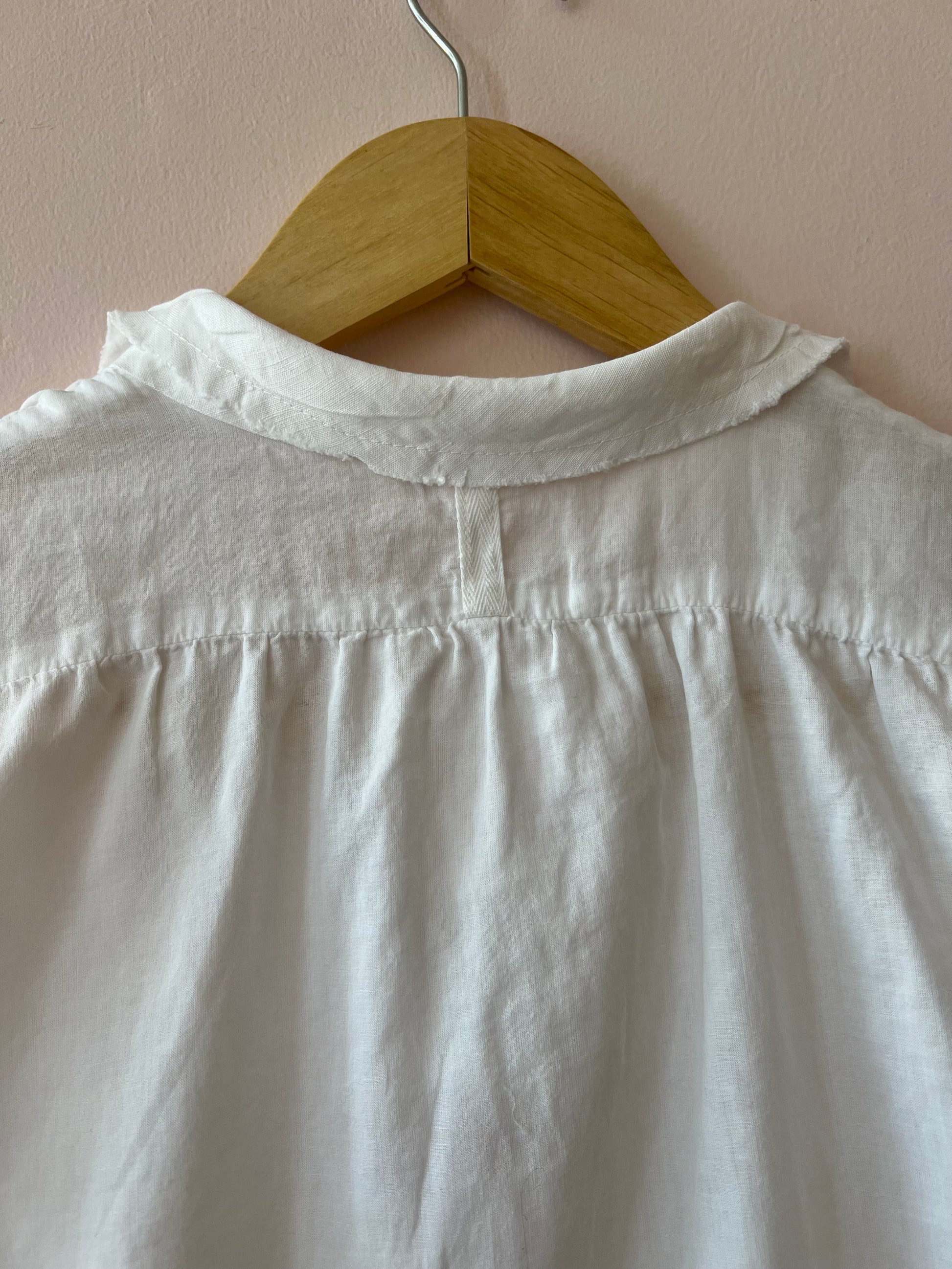 White shirt on a wooden hanger against a beige wall