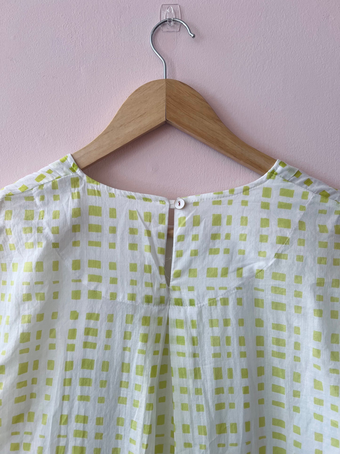 Green and white checkered dress on a wooden hanger against a light pink wall.