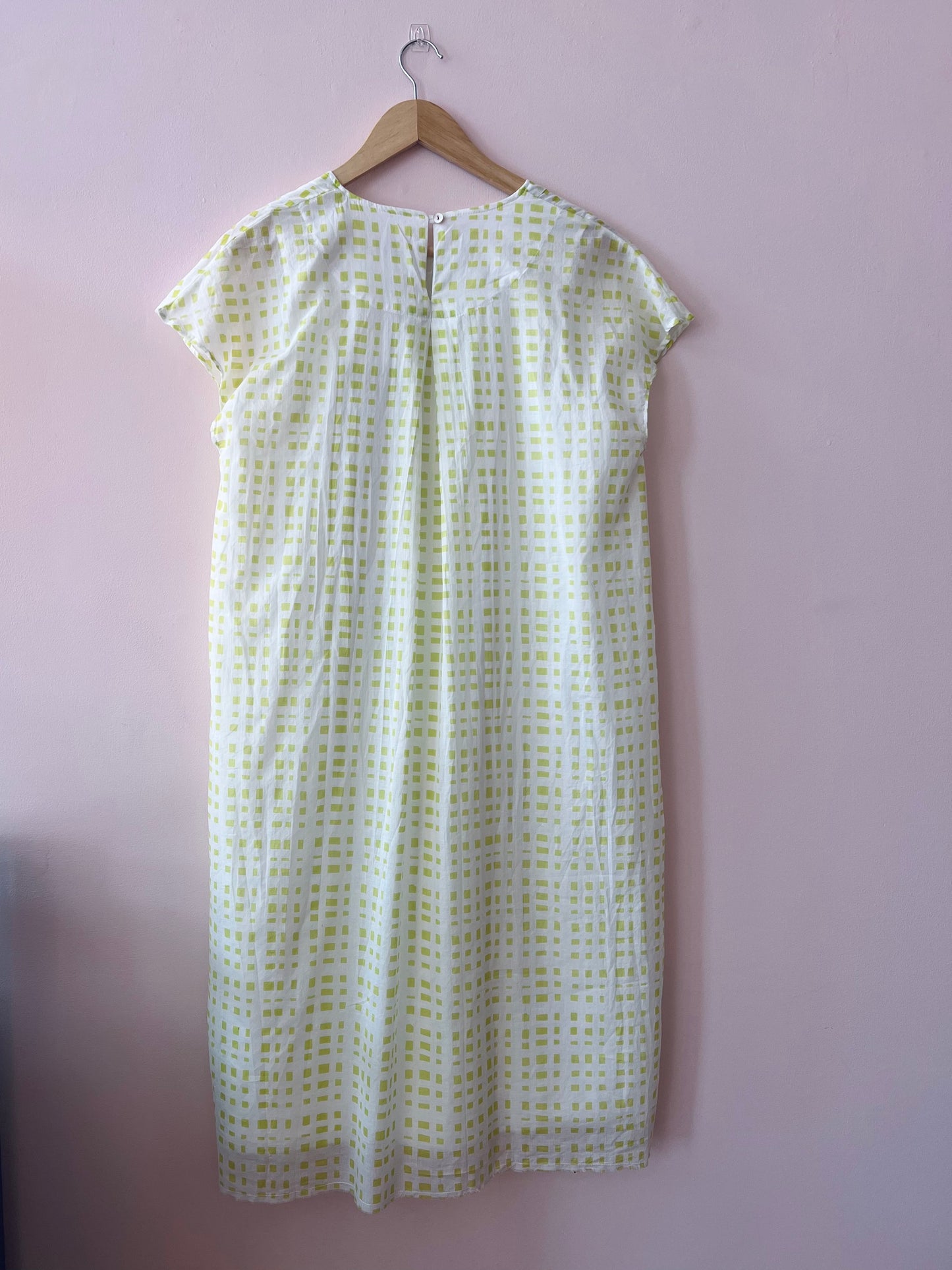 White dress with green pattern on a hanger against a purple wall
