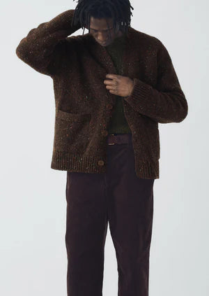Person wearing a brown knitted cardigan and dark pants on a white background