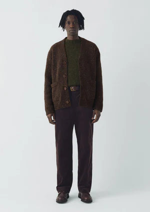 Man wearing a brown cardigan and dark pants on a white background