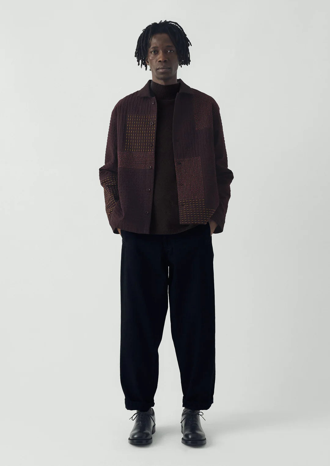 Man wearing a brown checkered jacket and black pants on a white background