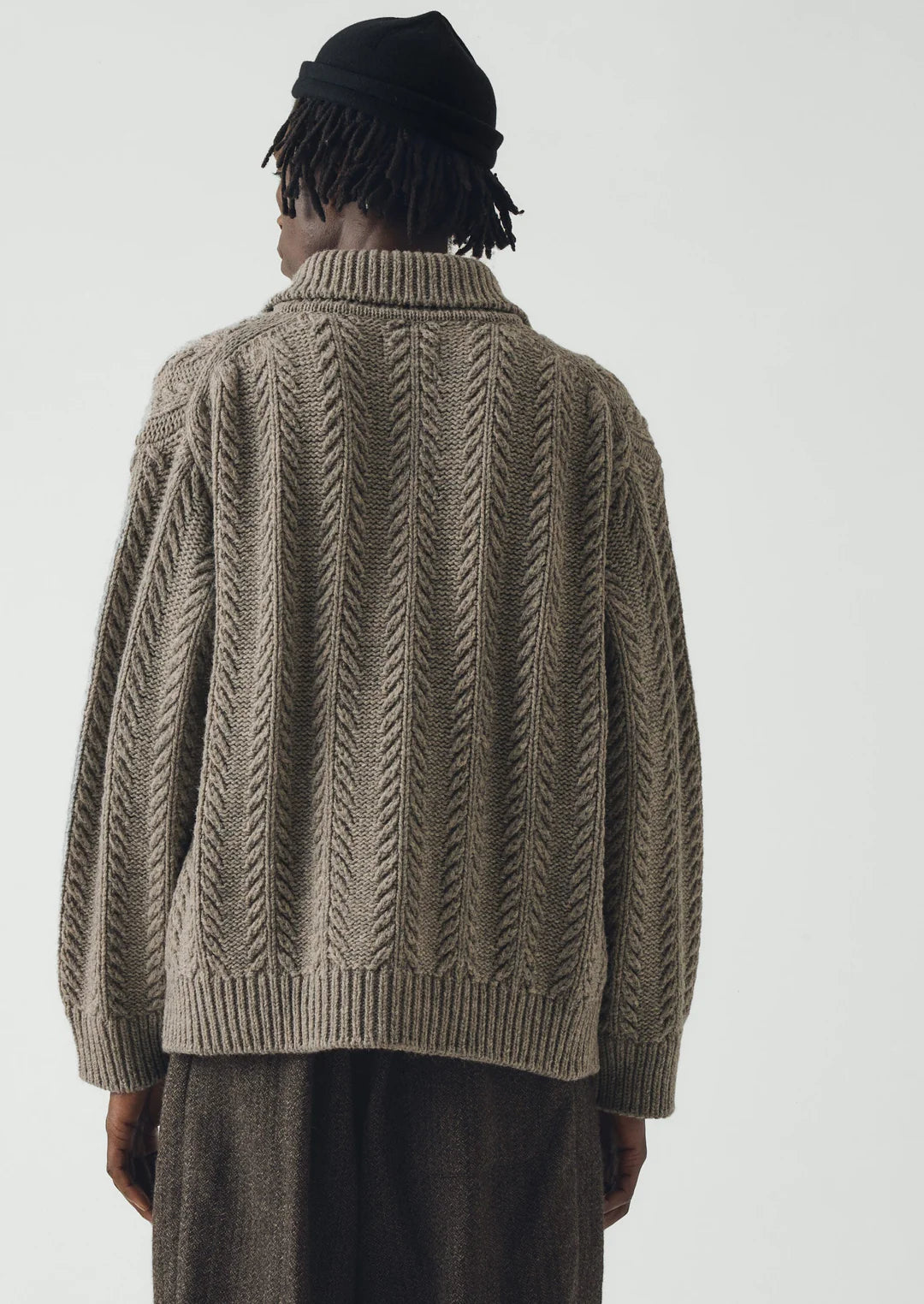 Rear view of a man wearing a beige colored heavy knitted wool cardigan and brown pants.