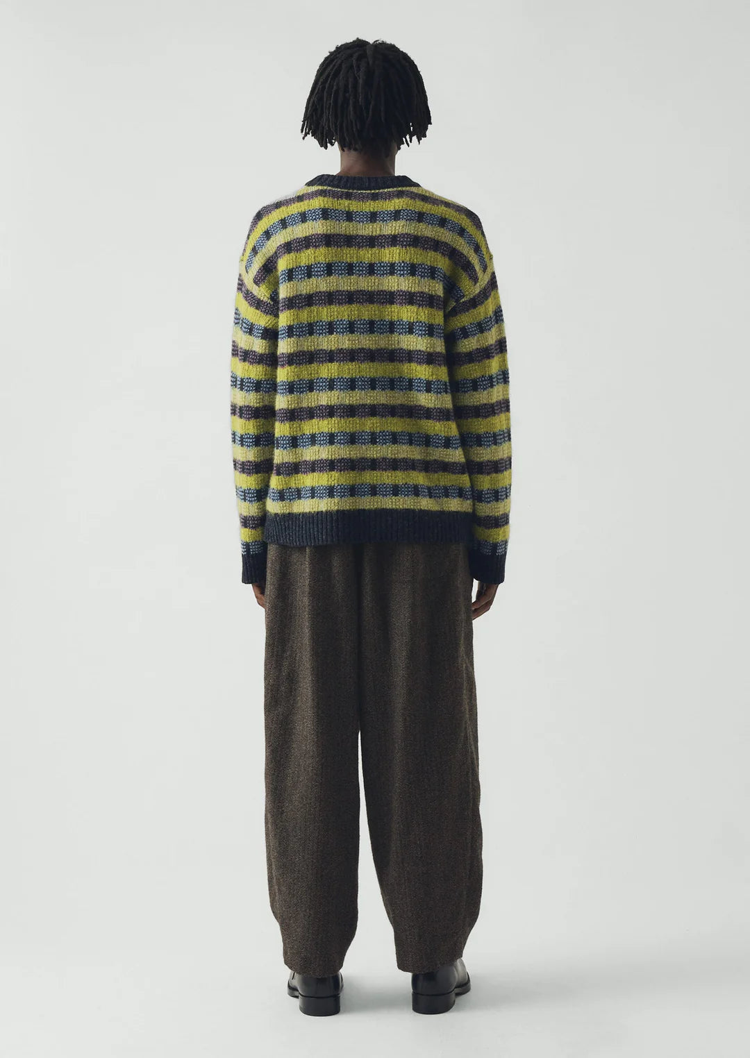 Person wearing a striped sweater and brown pants on a white background