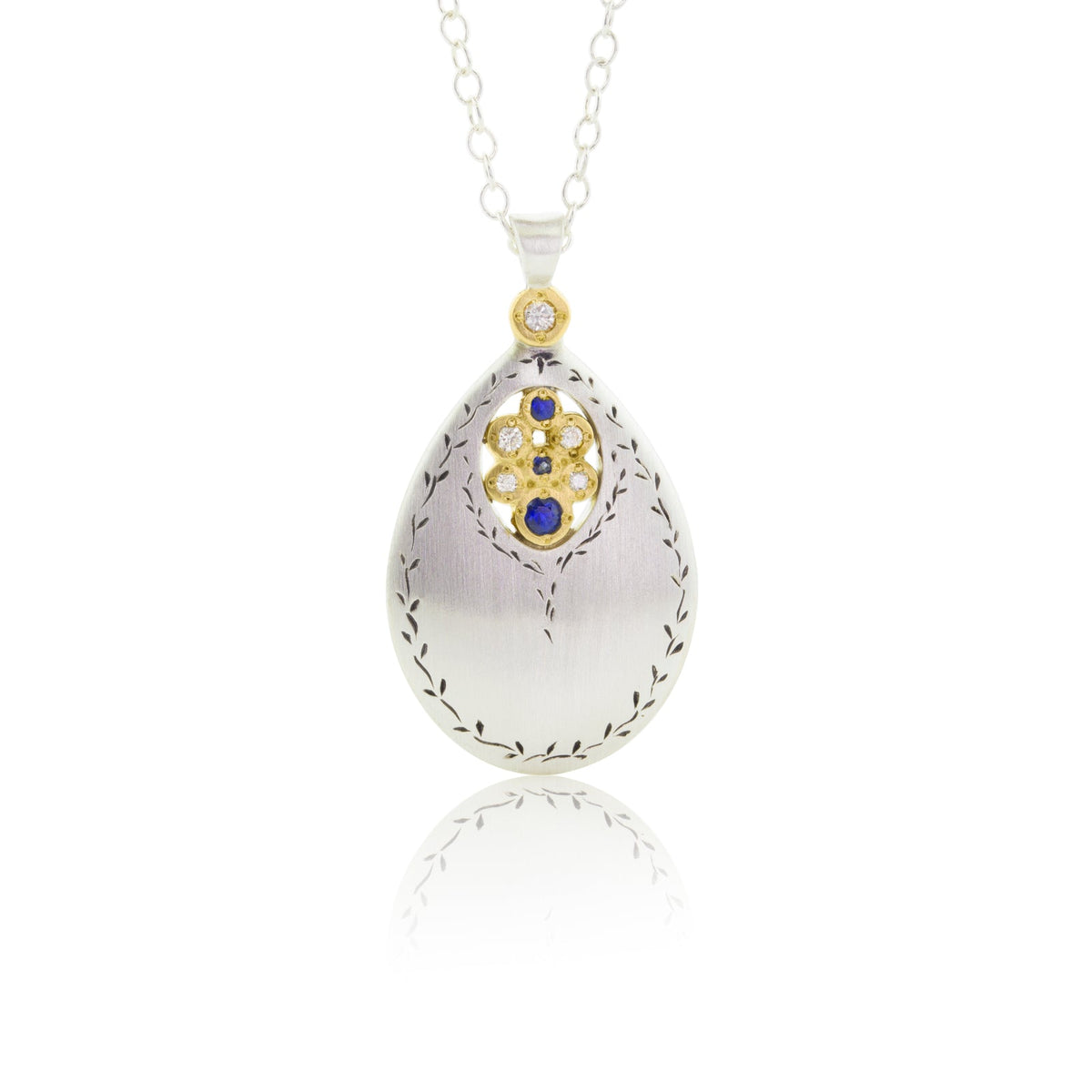 An engraved sterling silver pendant drops with a center of gemstones surrounded by yellow gold.