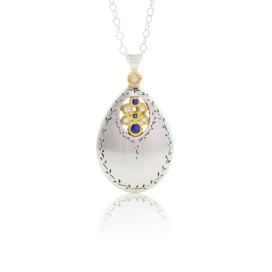 An engraved sterling silver pendant drops with a center of gemstones surrounded by yellow gold.
