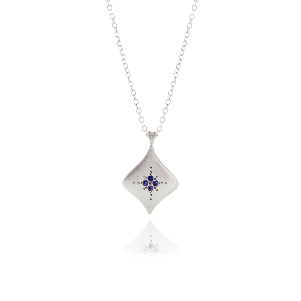 A sterling silver kite-shaped pendant necklace with an etched design and blue sapphires.