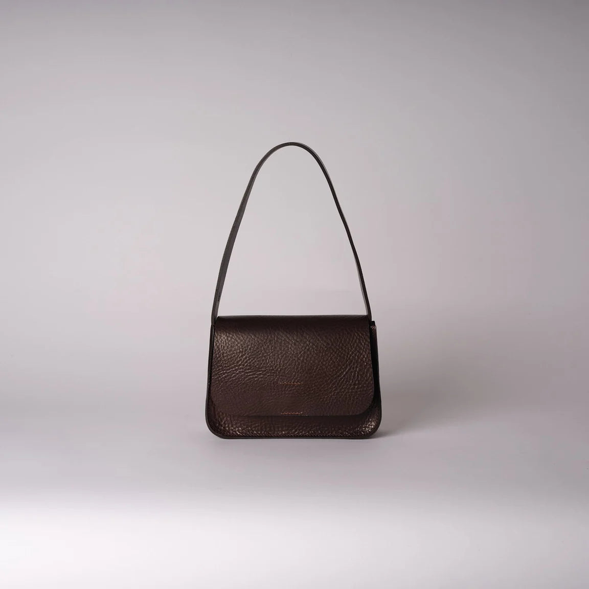 A dark brown textured leather shoulder bag with a slim matching leather strap, photographed against a neutral light gray studio background.