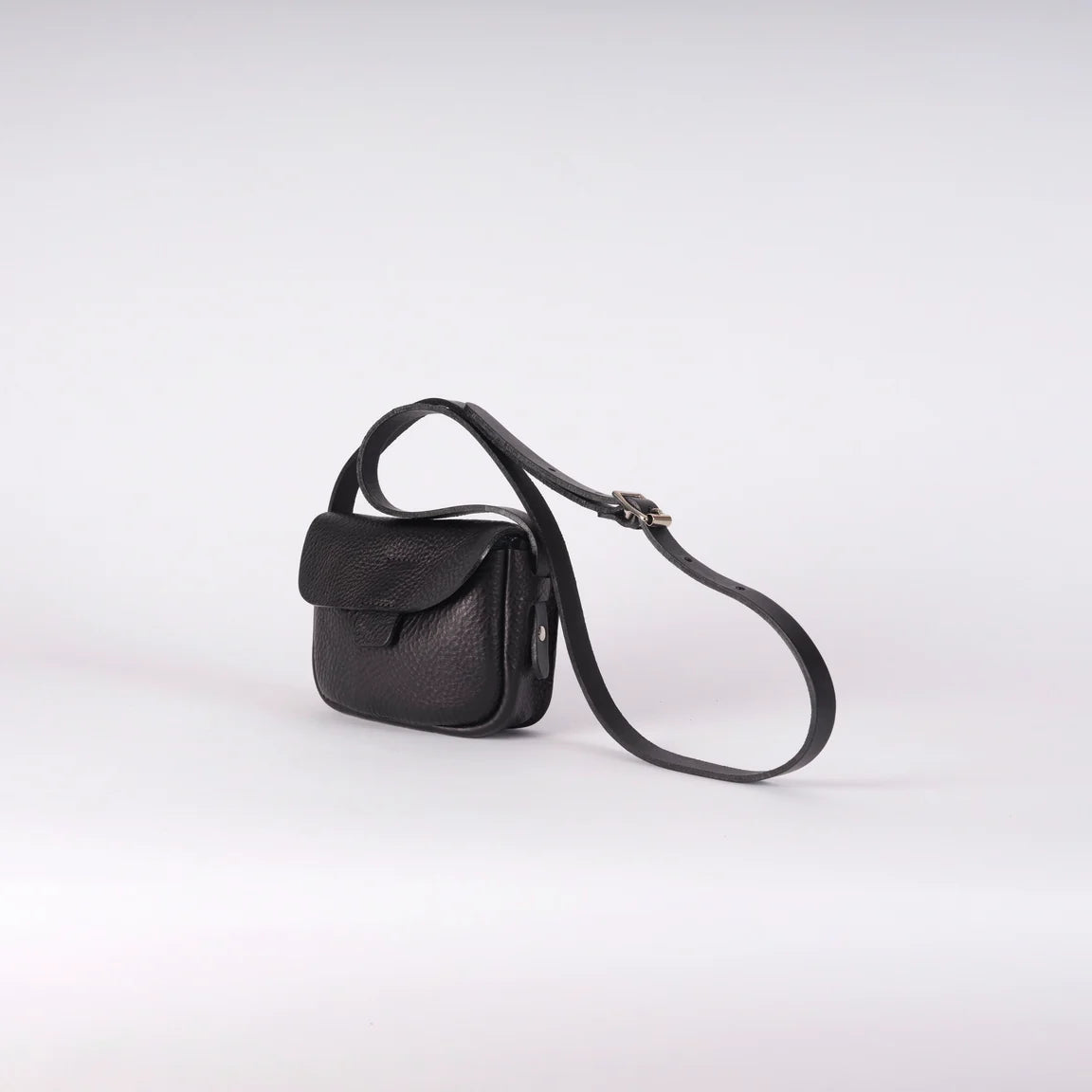 A small black leather crossbody bag with a long adjustable strap, shown on a light gray studio background.