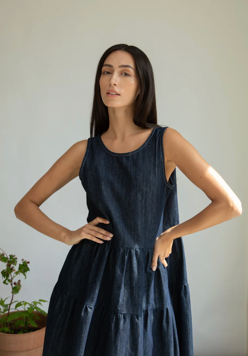 Woman wearing a dark blue sleeveless dress against a neutral background