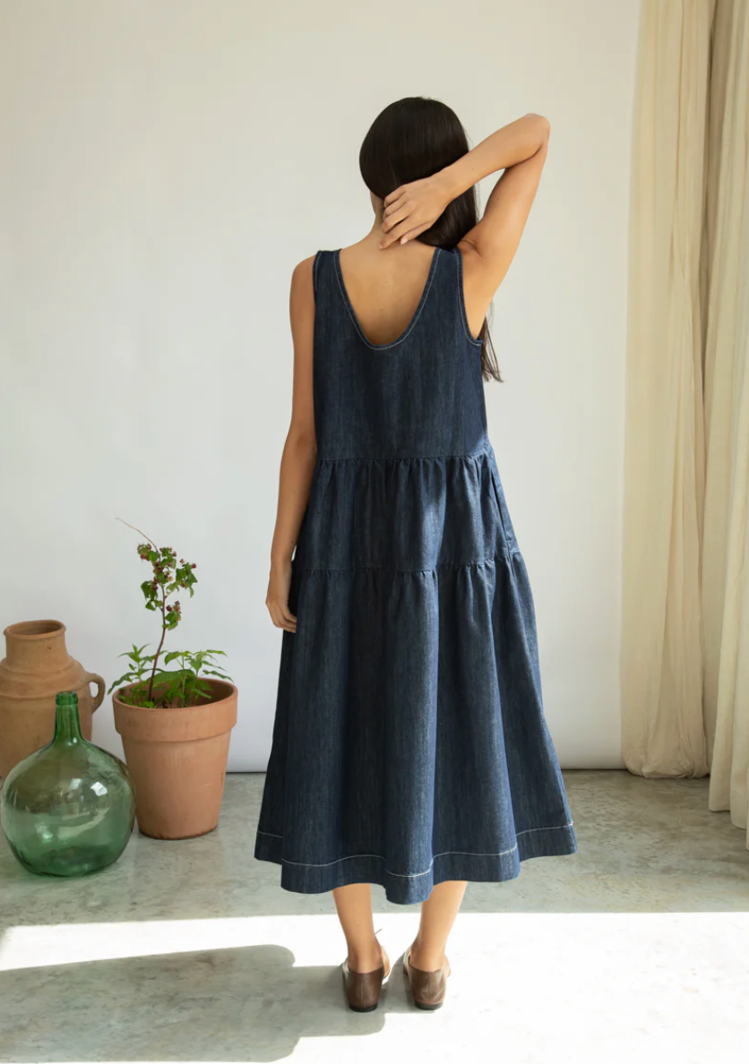 Woman wearing a dark blue dress standing in a room with plants and a curtain.