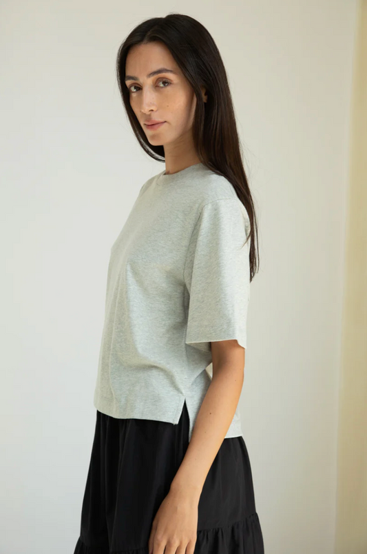 Woman wearing a light gray t-shirt and black skirt against a plain background