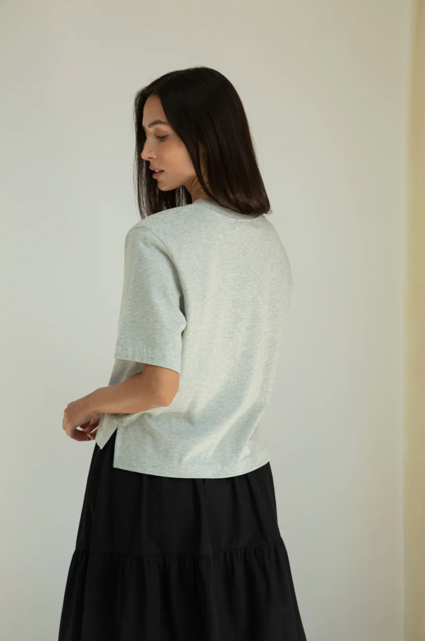 Woman wearing a light gray sweater and black skirt against a plain background