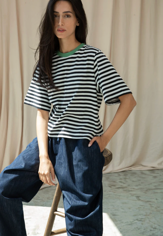 Woman wearing a black and white striped shirt and blue pants against a beige curtain background