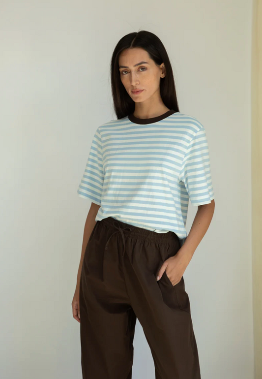 Woman wearing a striped shirt and brown pants against a plain background