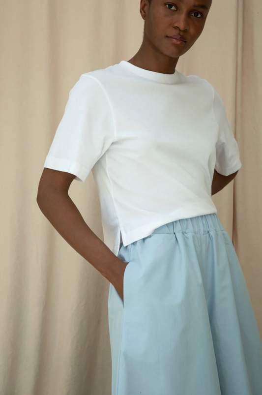 Person wearing a white top and light blue skirt against a beige background