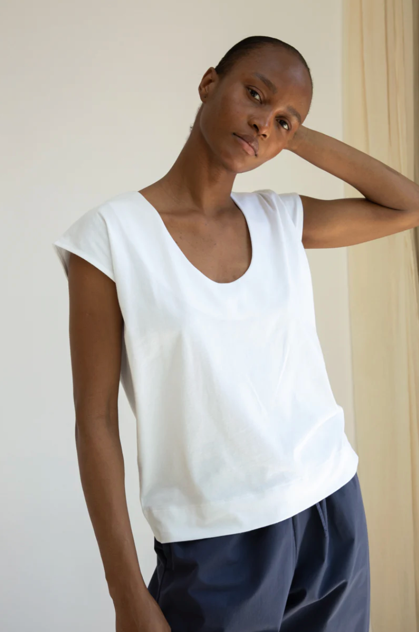 Woman wearing a white top and dark pants against a plain background