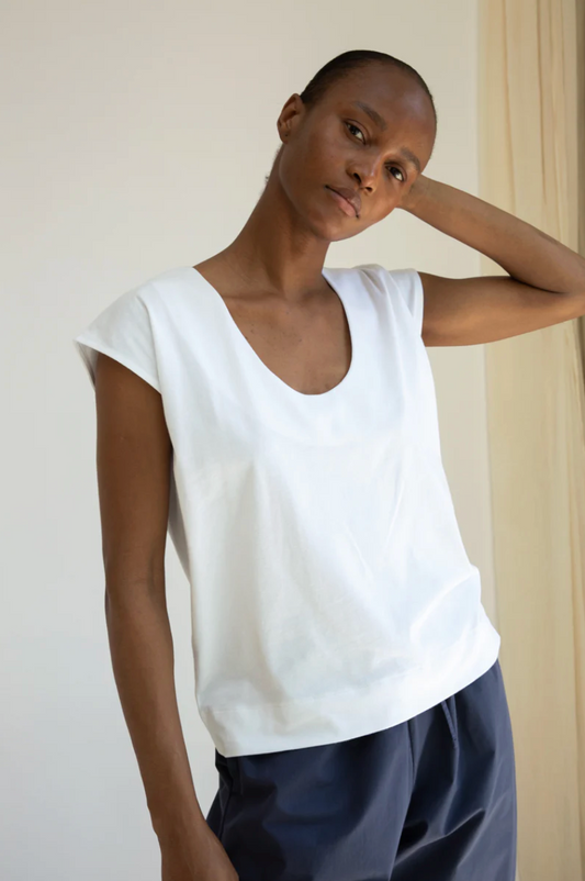 Woman wearing a white top and dark pants against a plain background