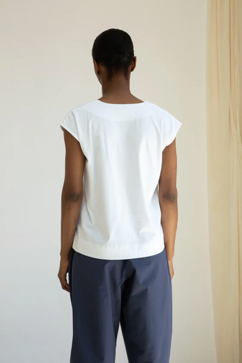 Person wearing a white top and dark pants against a plain background