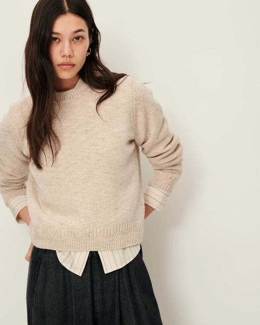 Woman wearing a beige sweater over a striped shirt with a plain background