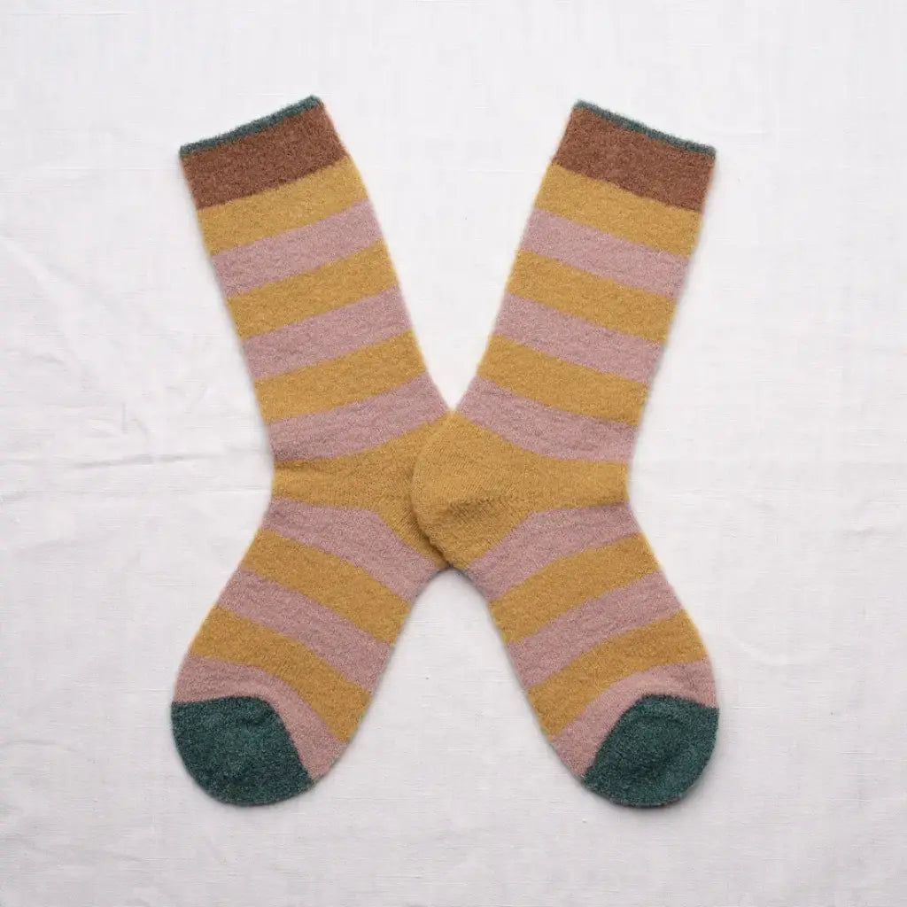 A pair of fluffy striped crew socks in an X shape on a white background. The sock stripes are a muted pink and yellow with brown and green cuffs and green toes.