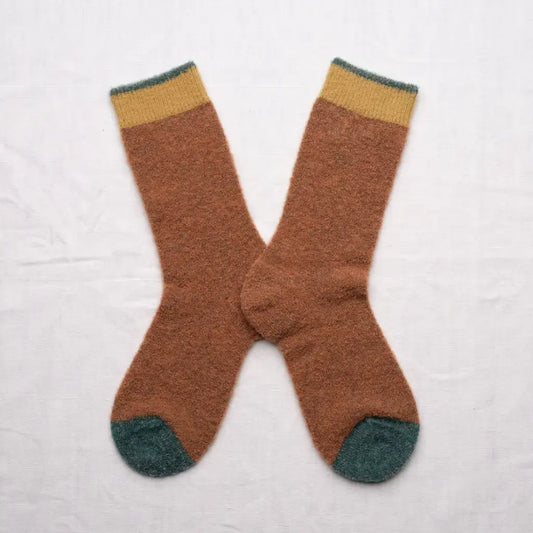 A pair of fluffy brown crew socks in an X shape on a white background. The soft brown socks have a muted yellow and green cuff with green toes.