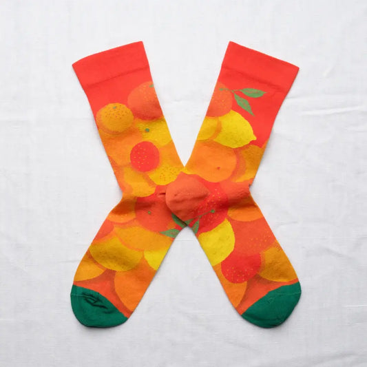 A pair of colorful crew socks in an X shape on a white background. The socks feature a group of citrus fruits on a vermillion background with green toes.