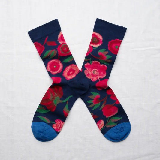 A pair of dark blue crew socks in an X shape on a white background. The socks have colorful pink flowers are on the navy background with cerulean blue toes.