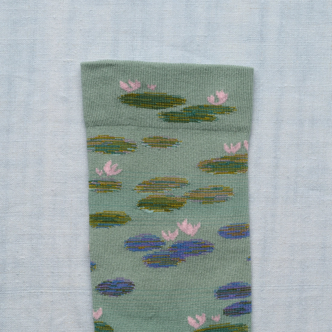A closeup photo of a  green sock with a monet water lily design.