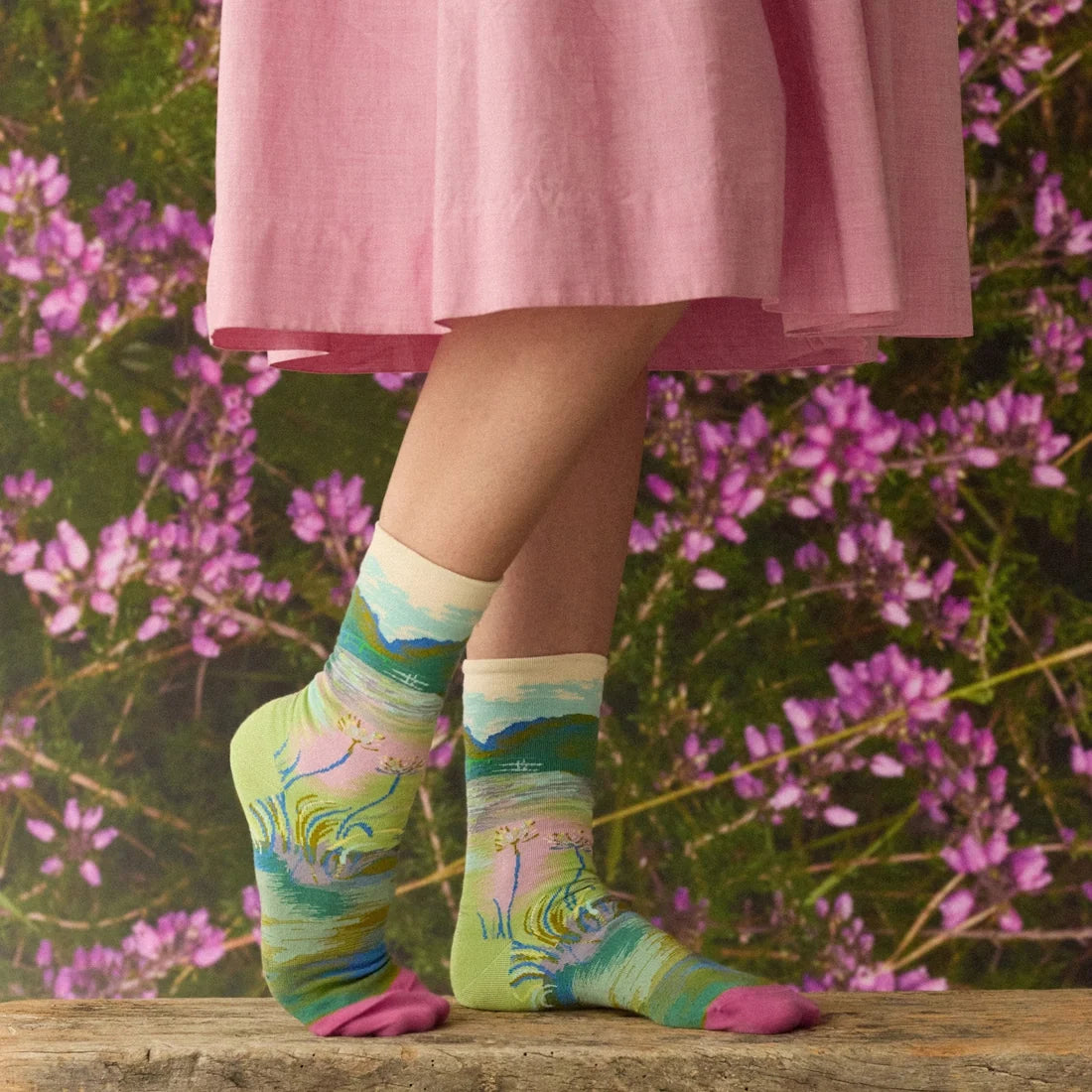A model wearing a pair of multicolor socks with a Monet bridge and water design and pink toes.