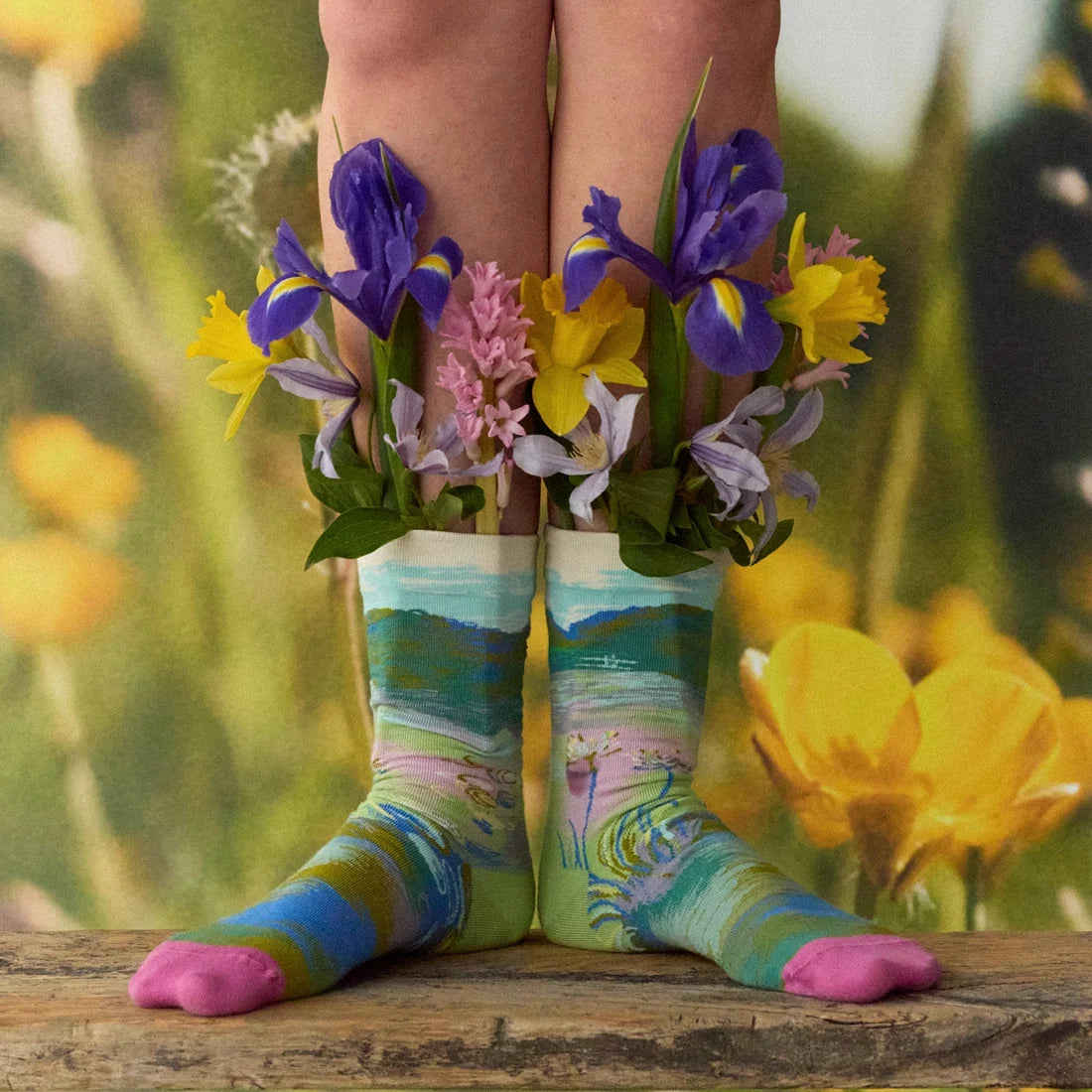 A model with flowers wearing a pair of multicolor socks with a Monet bridge and water design and pink toes.