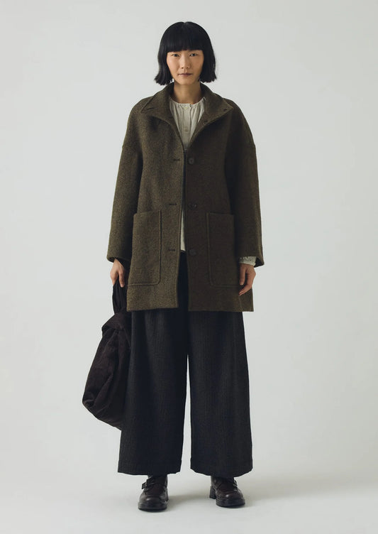Person wearing a long dark green coat and black pants on a white background