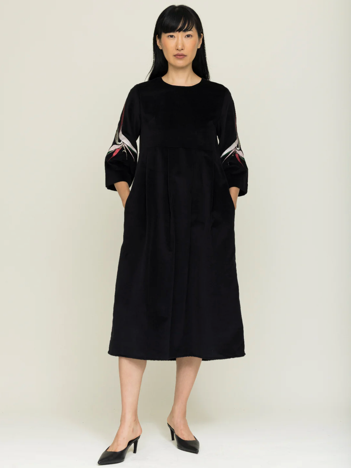 Woman wearing a black dress with colorful patterns on long sleeves against a white background