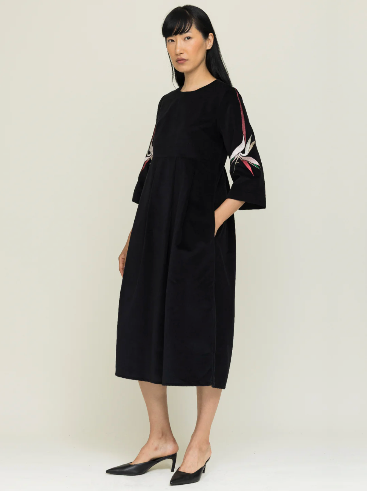 Woman wearing a black dress with floral sleeves against a plain background