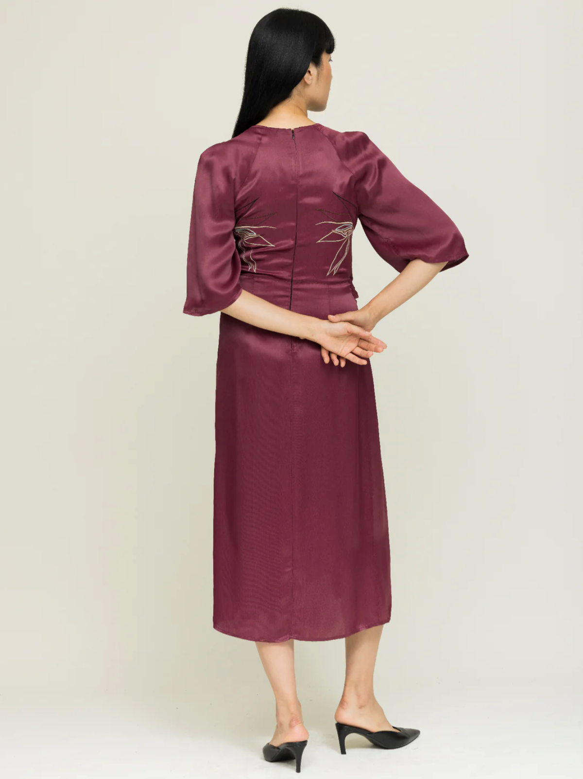 Woman wearing a burgundy dress with a subtle pattern on a plain background