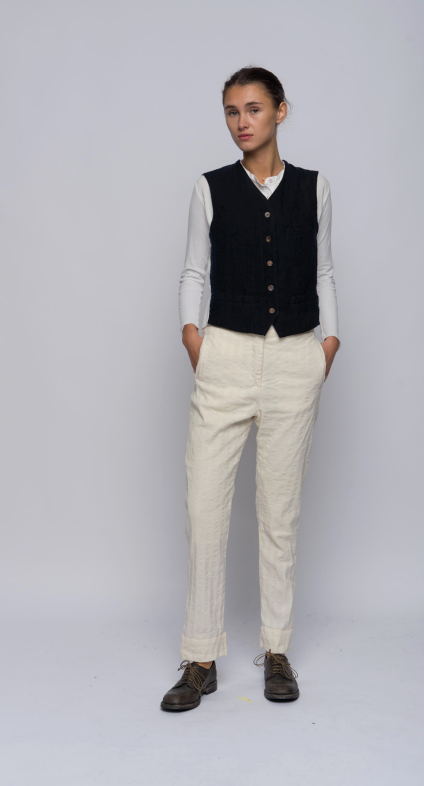 Model standing against a light grey background wearing a vest with two front welt pockets at waist. With a front button closure sewn with red thread.
