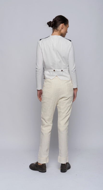 Model facing away and standing against a light grey background wearing a vest with two front welt pockets at waist. With a front button closure sewn with red thread. The back is a white color.
