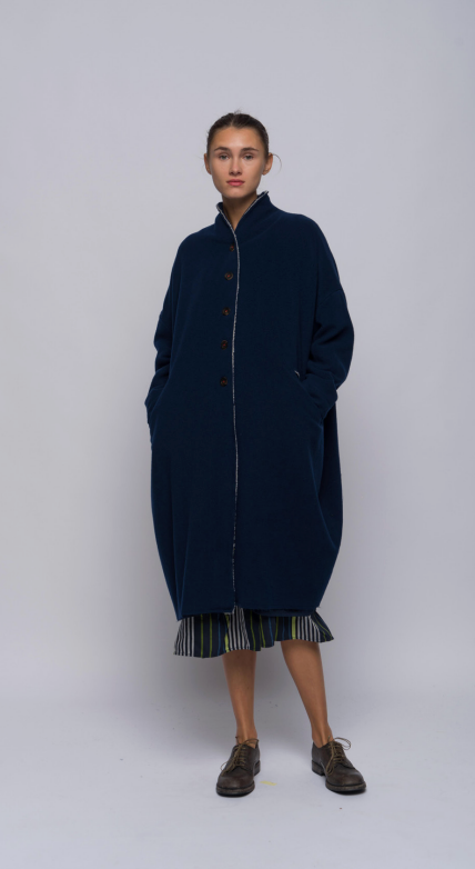 Woman standing in a wool and cashmere blend coat in inky blue. Features dropped shoulders, front pockets and cashmere knit cuffs.