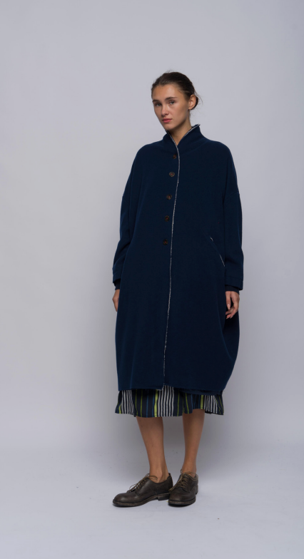 Woman standing in a wool and cashmere blend coat in inky blue. Features dropped shoulders, front pockets and cashmere knit cuffs.
