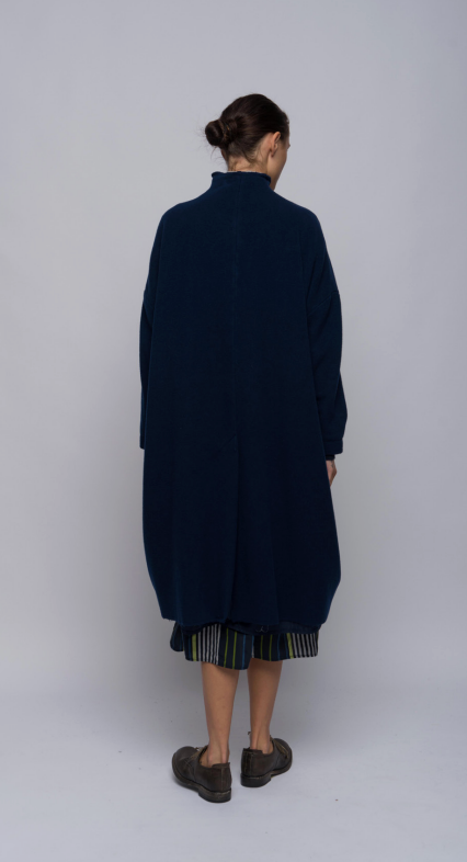 Looking at the back, a woman standing in a wool and cashmere blend coat in inky blue. Features dropped shoulders, front pockets and cashmere knit cuffs.