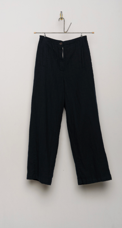 Black wide-leg cropped pants hanging from a metal hanger against a plain off-white wall.