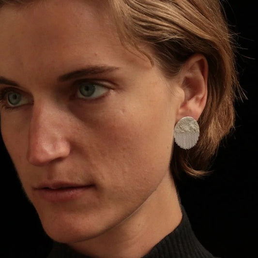 A close up photo of a woman wearing round silver post earrings with fringed details