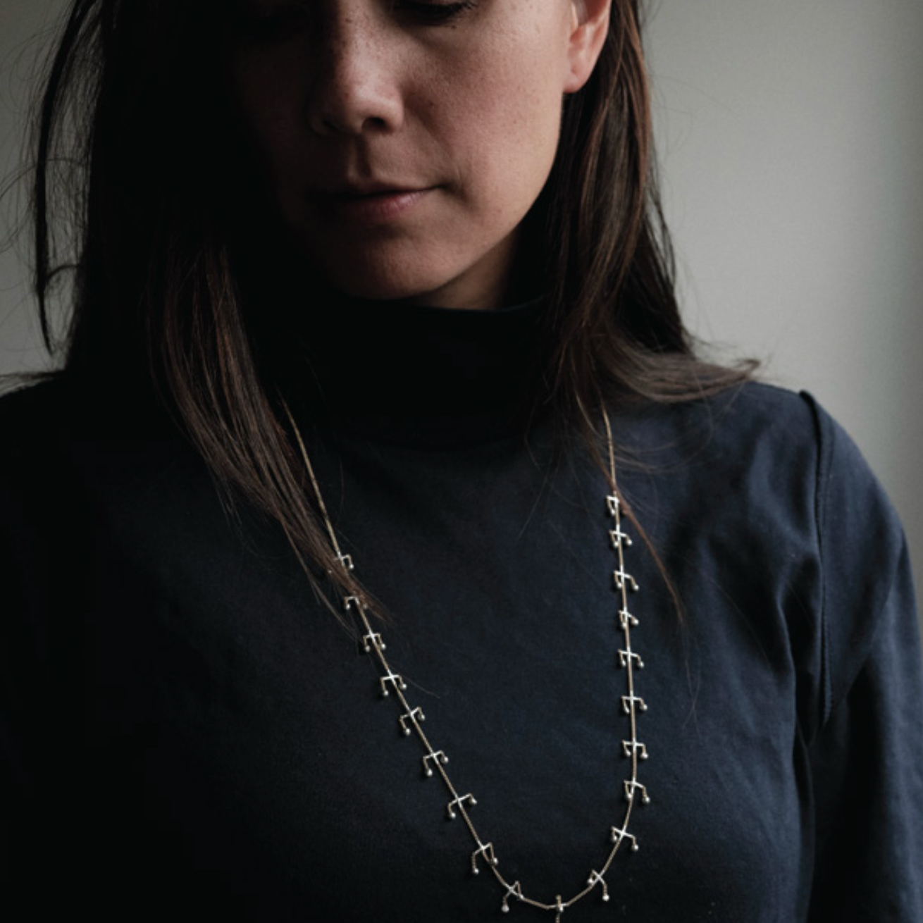 Person wearing a long necklace with a dark background