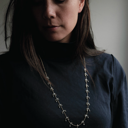 Person wearing a long necklace with a dark background