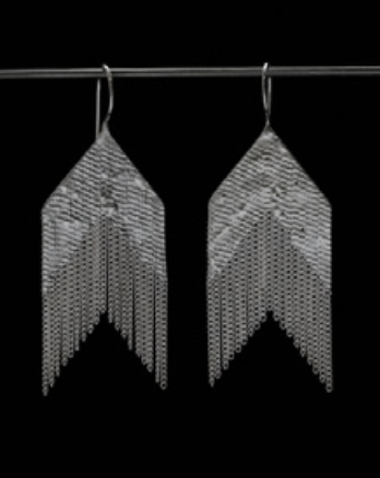 A pair of silver-toned geometric dangle earrings with a textured chevron pattern and hanging fringe, displayed against a solid black background.