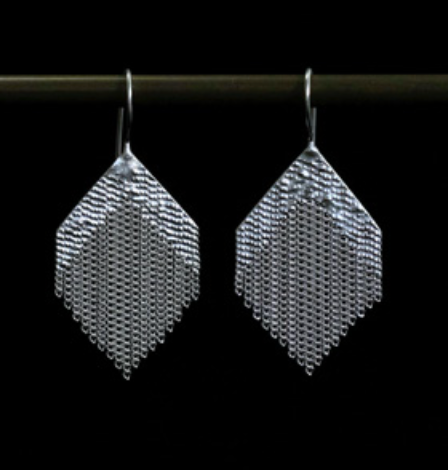 A pair of silver geometric dangle earrings with a textured mesh-like diamond shape and dangling chain details, shown hanging from a dark rod against a black background.