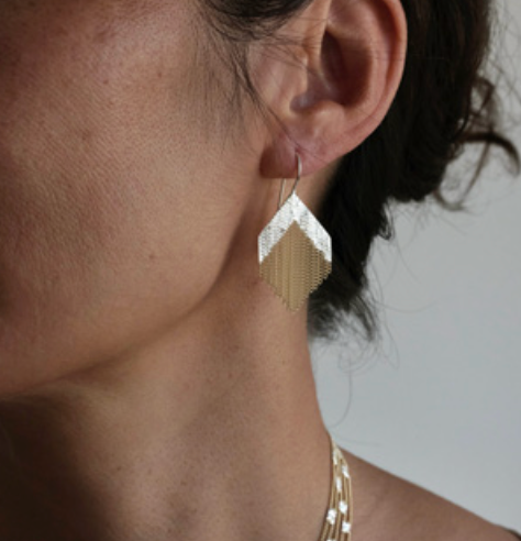 A woman wears an earring in a diamond-shape with silver and brass chains.