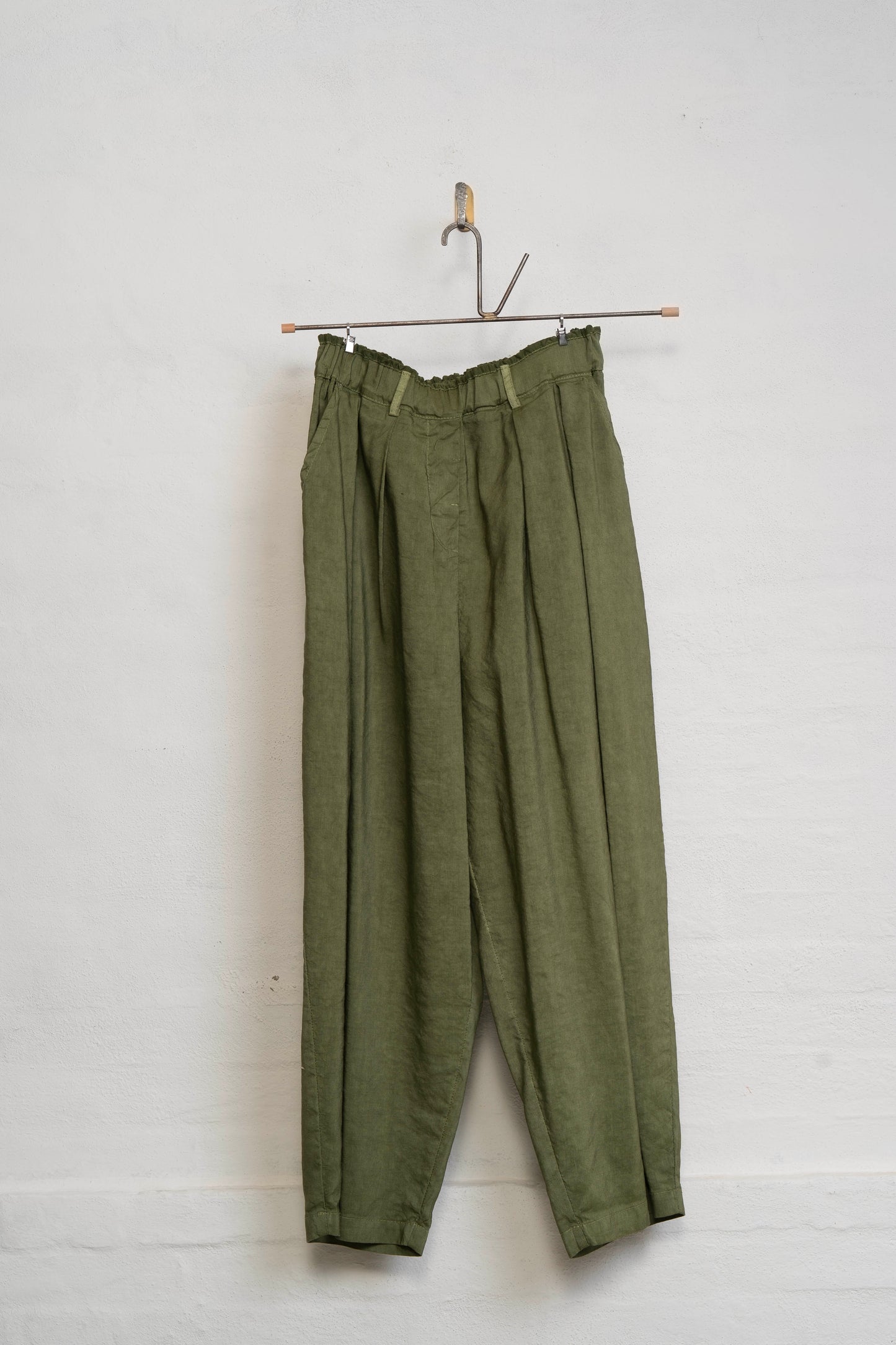 Green pants hanging on a hook against a white wall