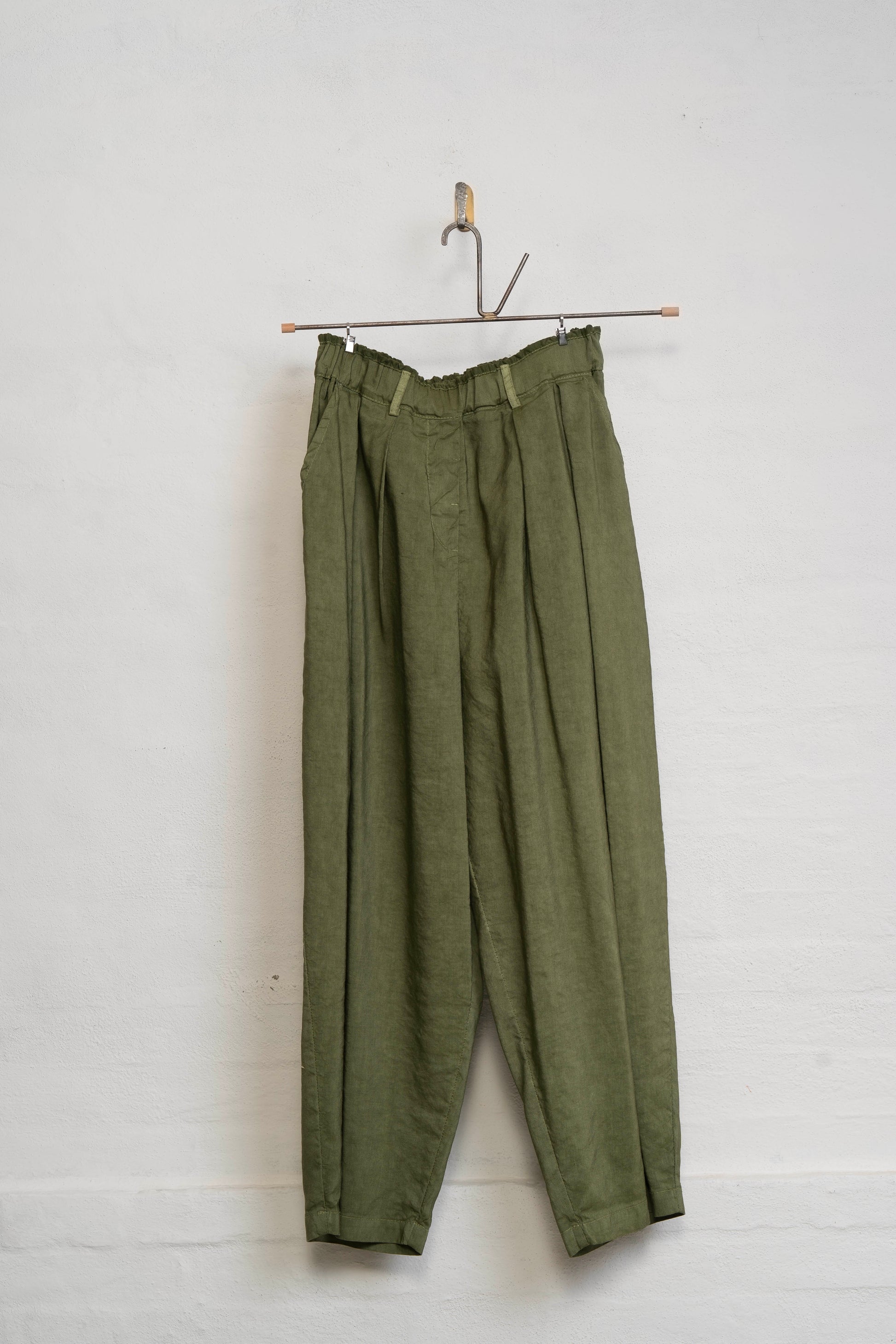 Green pants hanging on a hook against a white wall